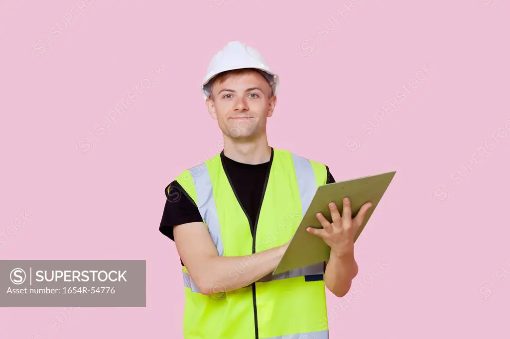Portrait of a male construction worker with clipboard over pink background
