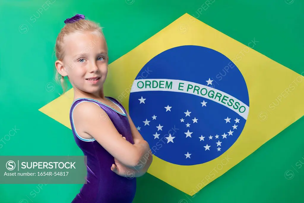 Portrait of a happy young female gymnast with arms crossed standing in front of South American flag