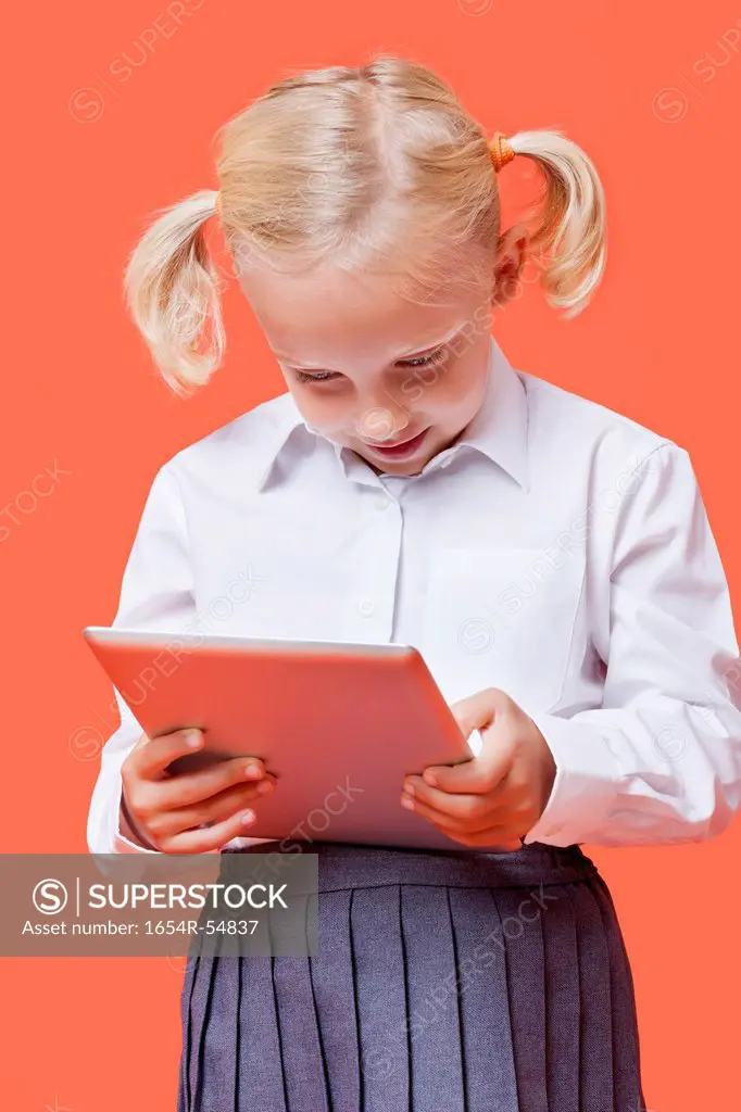 Happy young schoolgirl using tablet PC over orange background
