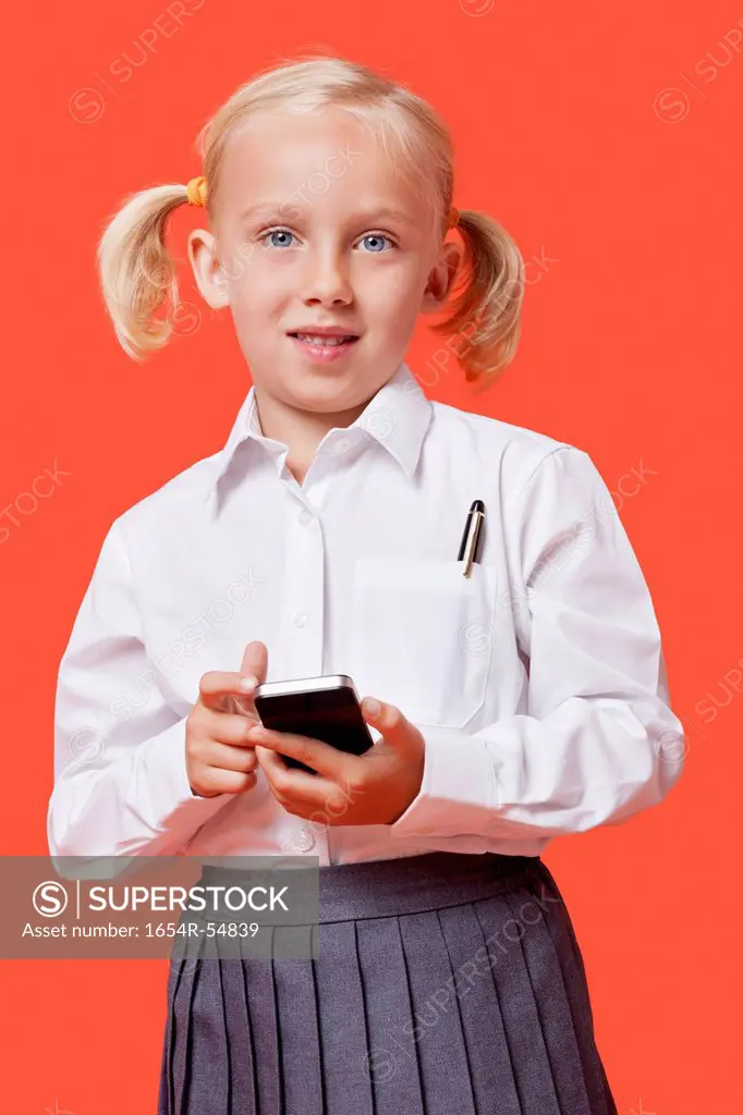 Portrait of a young schoolgirl holding cell phone over blue background