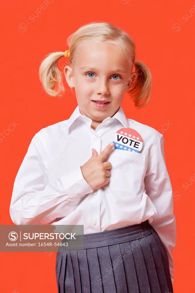 Portrait of a young school girl with vote badge over orange background