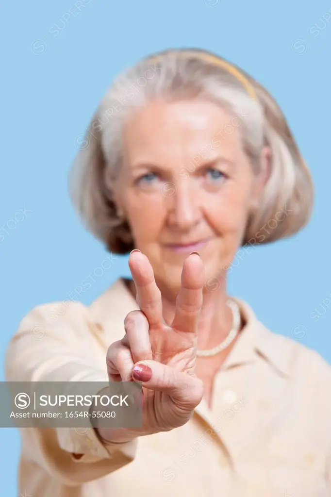Portrait of senior woman in casuals gesturing peace sign against blue background