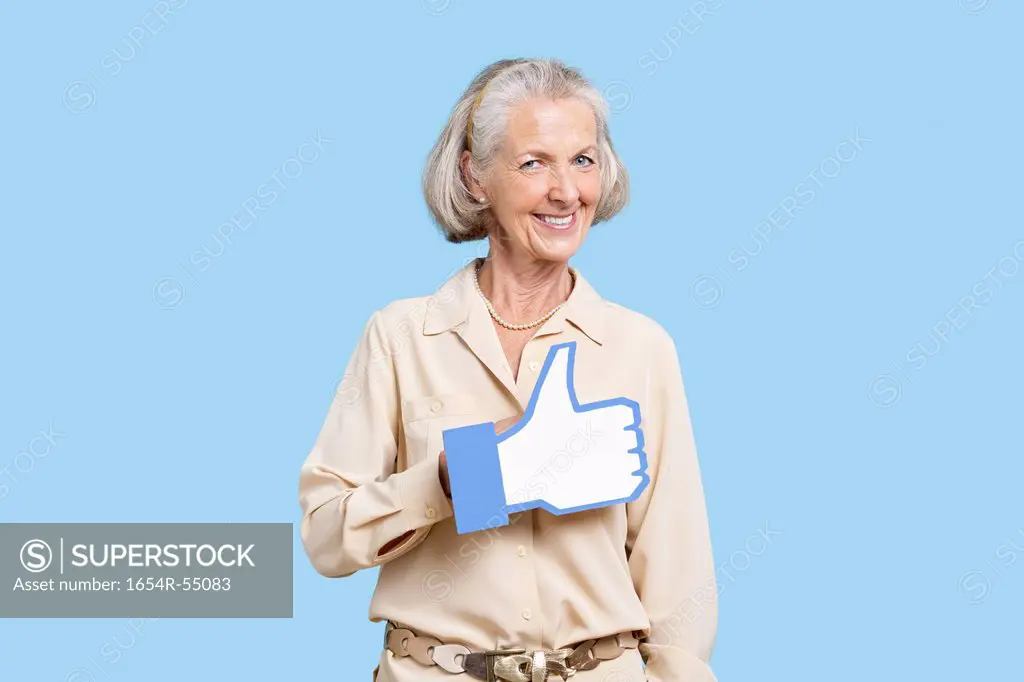 Portrait of senior woman in casuals holding fake like button against blue background