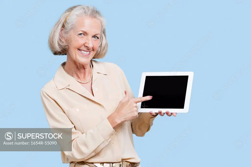 Portrait of senior woman showing tablet PC against blue background