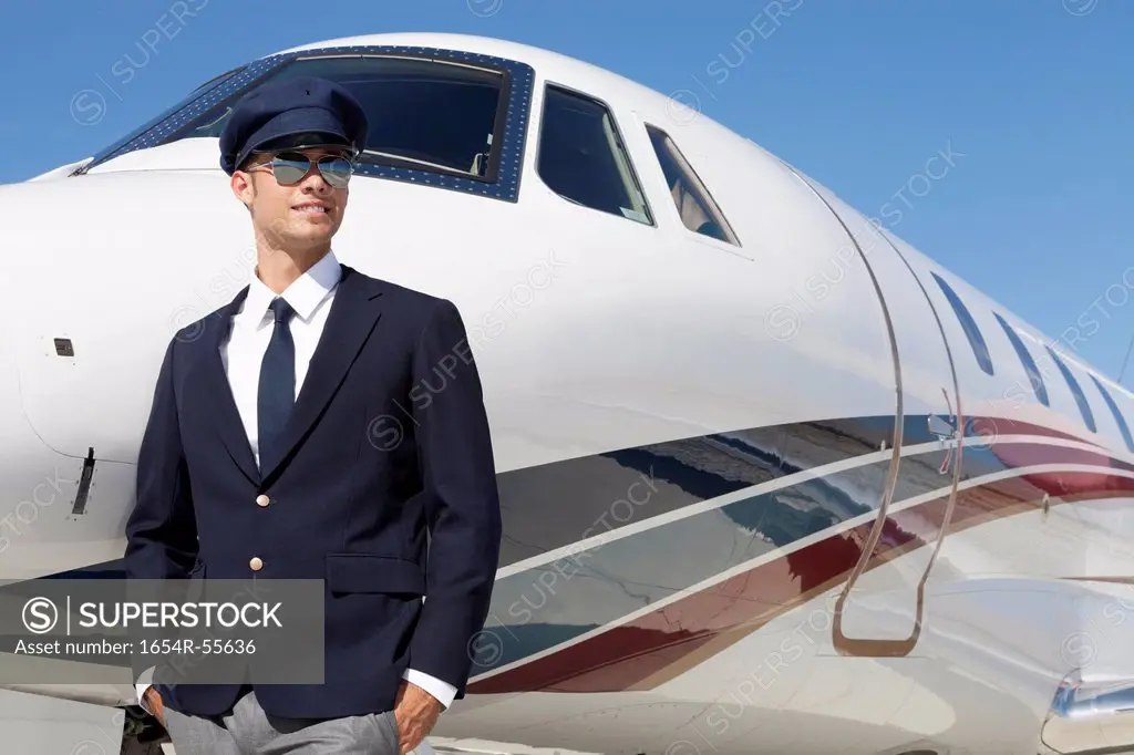 Handsome young pilot standing by private airplane