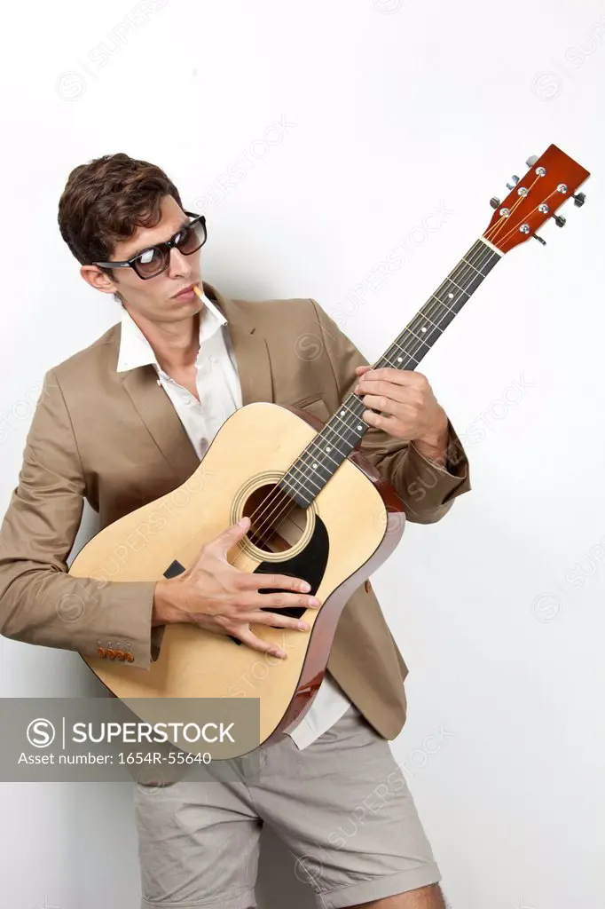 Young man smoking while playing guitar against white background