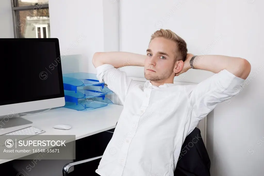Portrait of young businessman relaxing on chair at office desk
