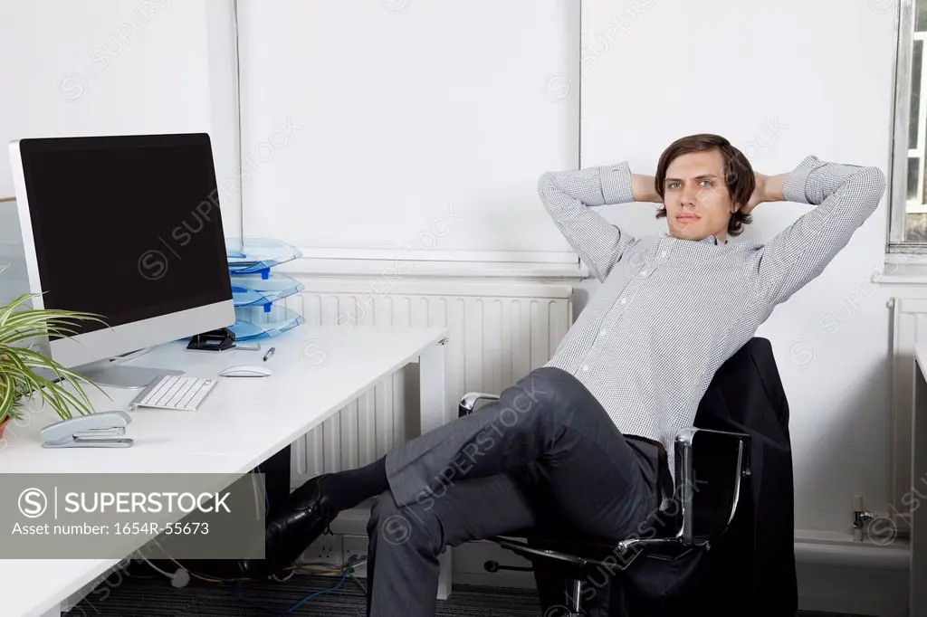 Portrait of young businessman relaxing on chair with hands behind head in office