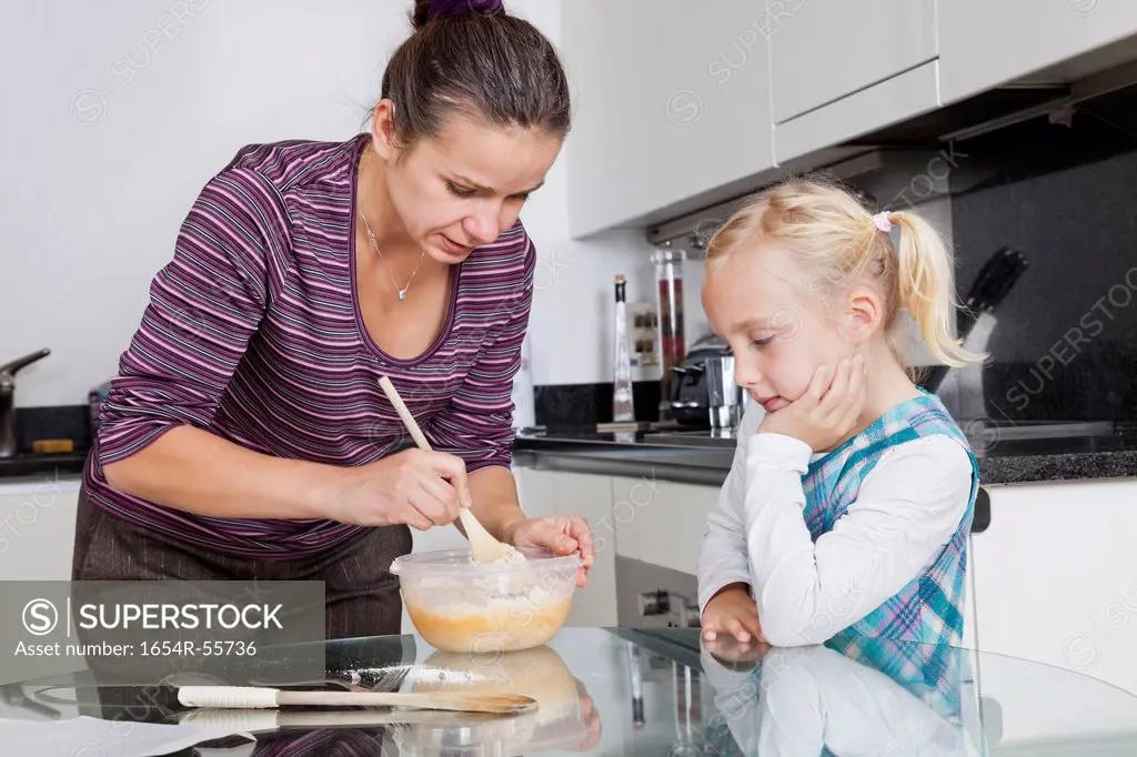 Girl looking at mother cooking in kitchen