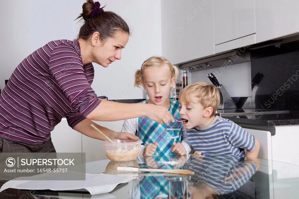 Mother with children baking and tasting cookie batter in kitchen