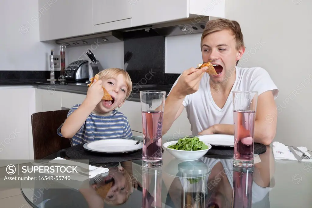 Father and son eating pizza at breakfast table