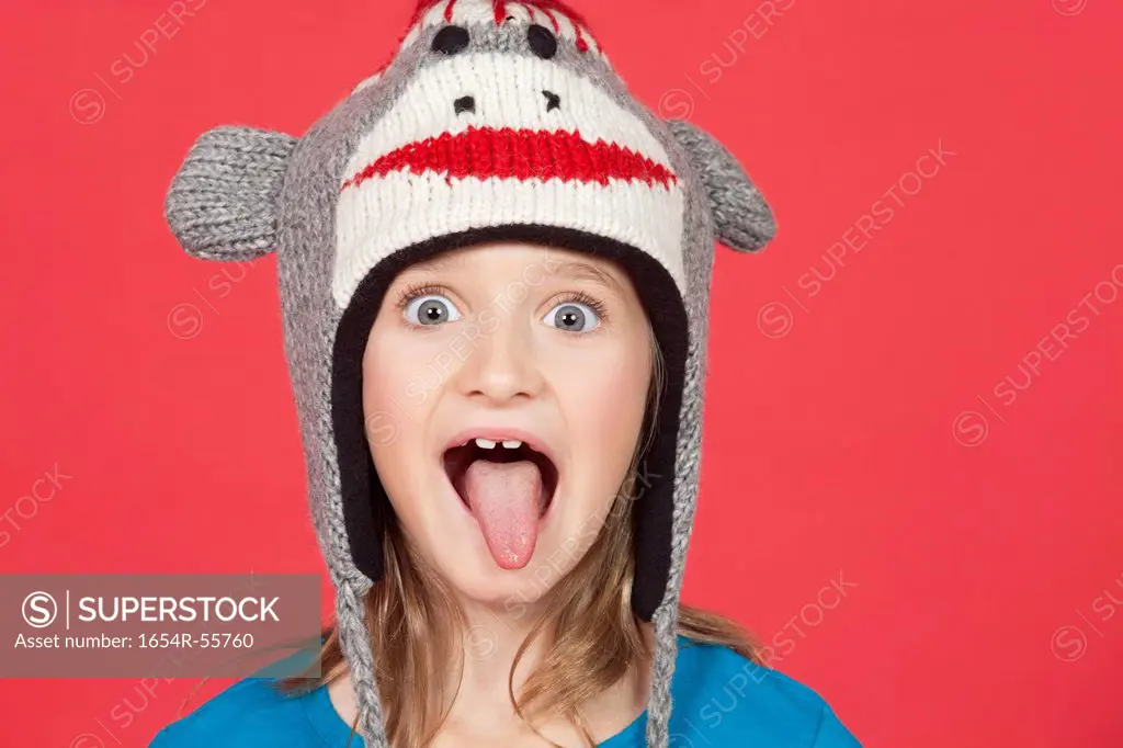 Portrait of girl sticking out tongue against red background