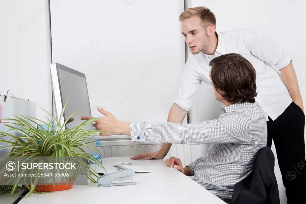 Businessman showing computer screen to coworker at desk