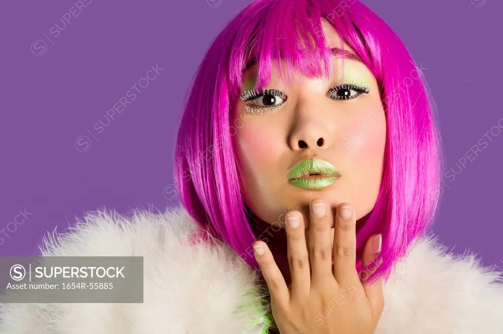 Portrait of young funky woman in pink wig blowing kiss over purple background