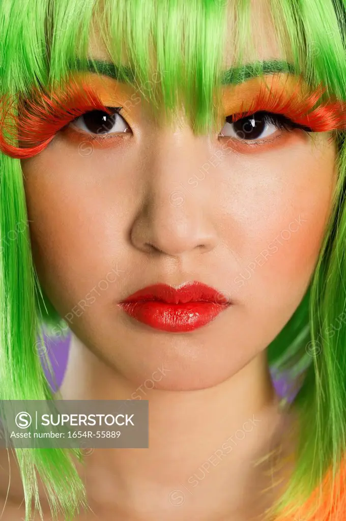 Close_up portrait of young woman wearing green wig and orange eyelashes over gray background