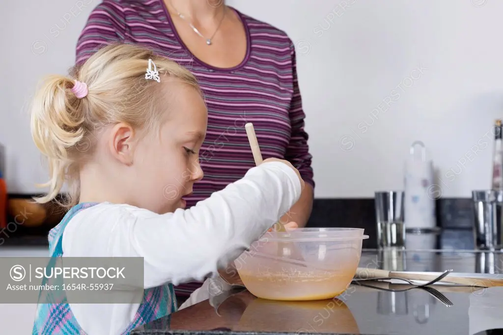 Girl and mother cooking together in kitchen