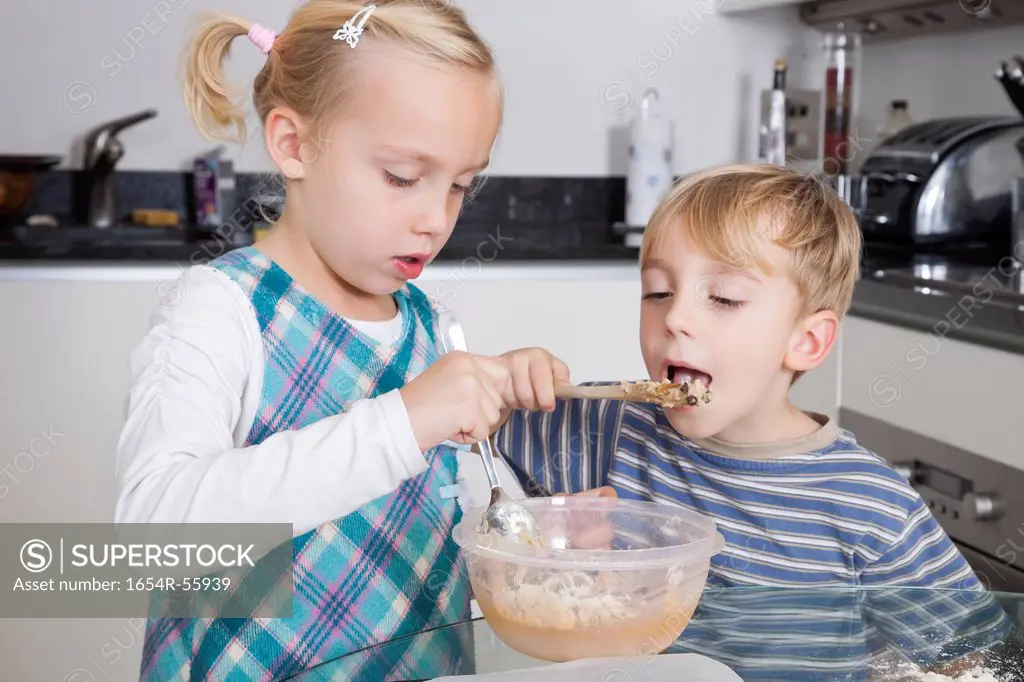 Girl baking cookie while brother tasting batter in kitchen