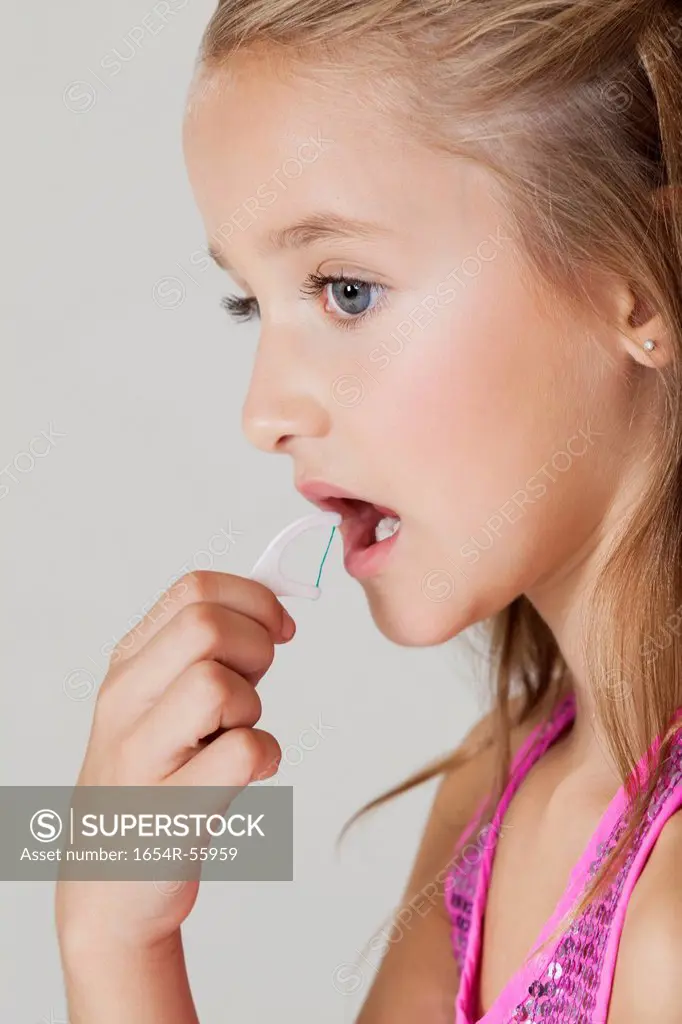 Young girl flossing teeth against gray background