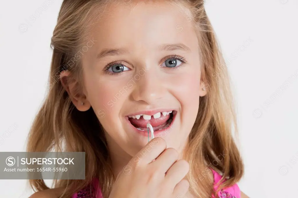 Portrait of young girl flossing teeth against gray background