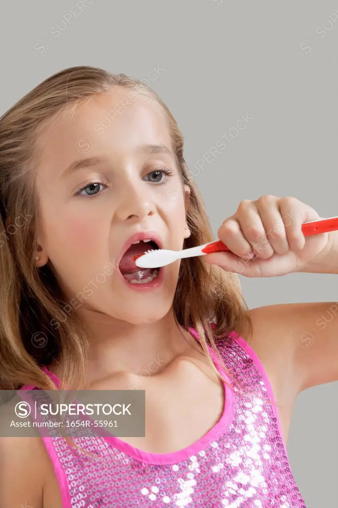 Young girl brushing teeth against gray background