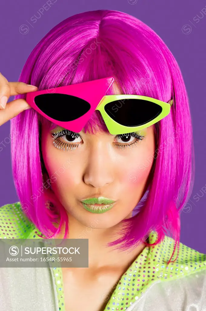 Portrait of young funky woman in pink wig puckering lips over purple background