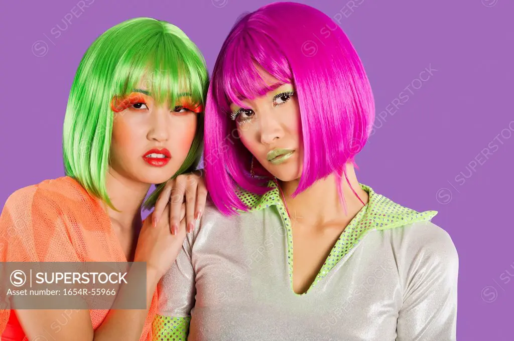 Portrait of two female friends wearing wigs against gray background