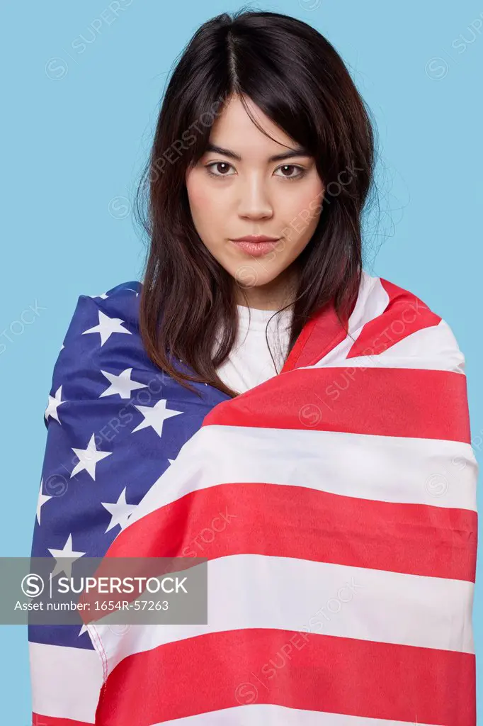 Patriotic young woman wrapped in American flag over blue background