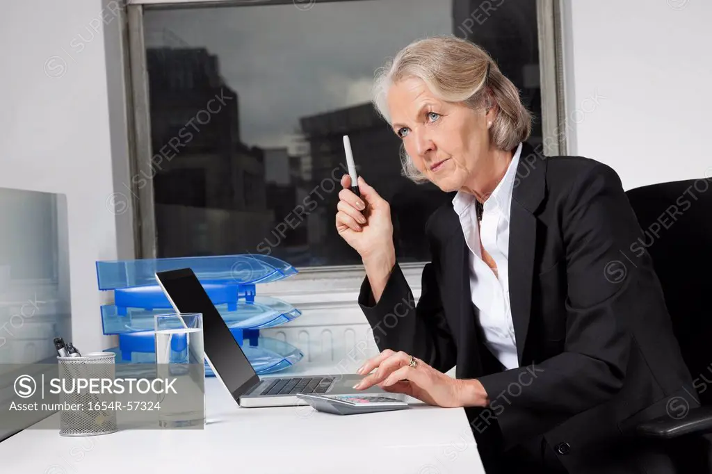 Senior businesswoman using laptop and calculator at desk in office