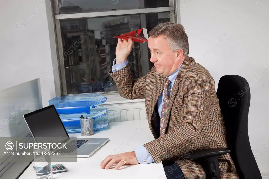 Side view of middle_aged businessman throwing paper airplane in office