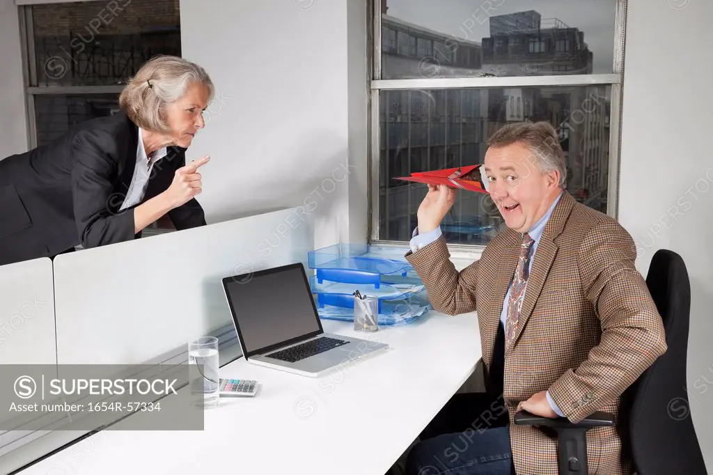 Middle_aged businessman throwing paper airplane towards female colleague in office