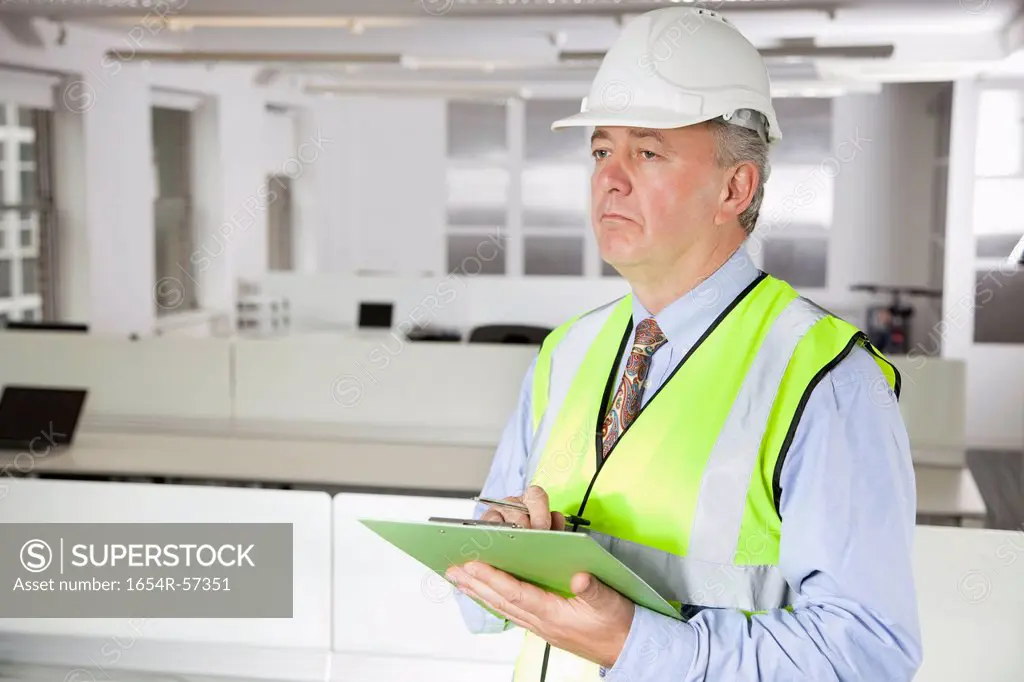 Middle_aged man in reflector vest and hard hat with clipboard at office