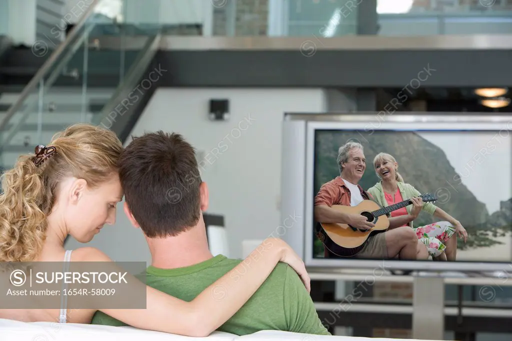 Rear view of young couple watching television in living room