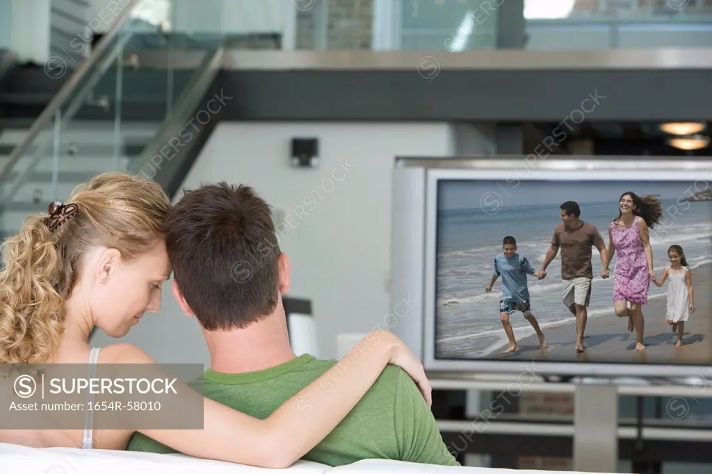 Rear view of young couple watching television in living room