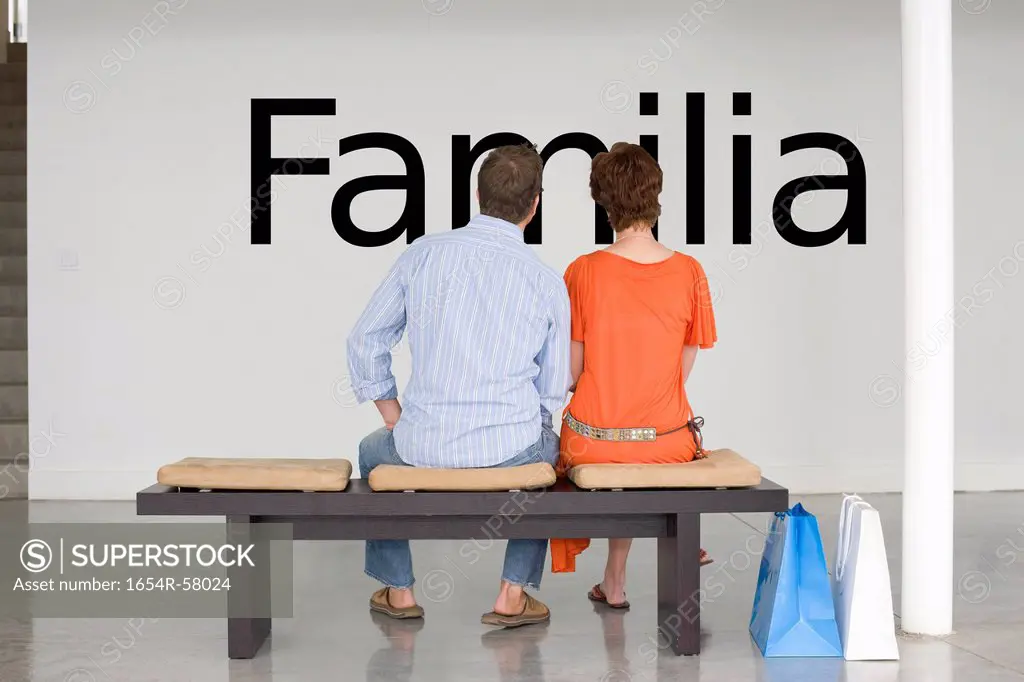 Rear view of couple seated on bench reading Spanish text Familia family on wall