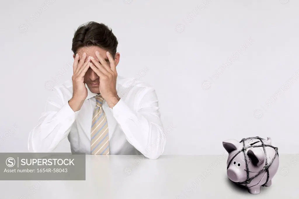 Worried businessman at table with trapped piggy bank representing financial difficulties