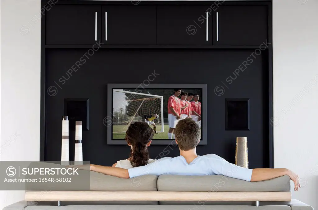 Back view of couple watching soccer game on television in living room