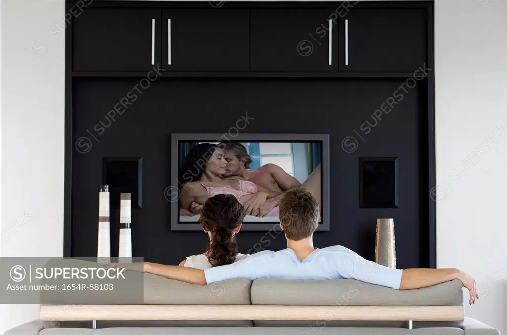 Back view of couple watching romantic movie on television in living room