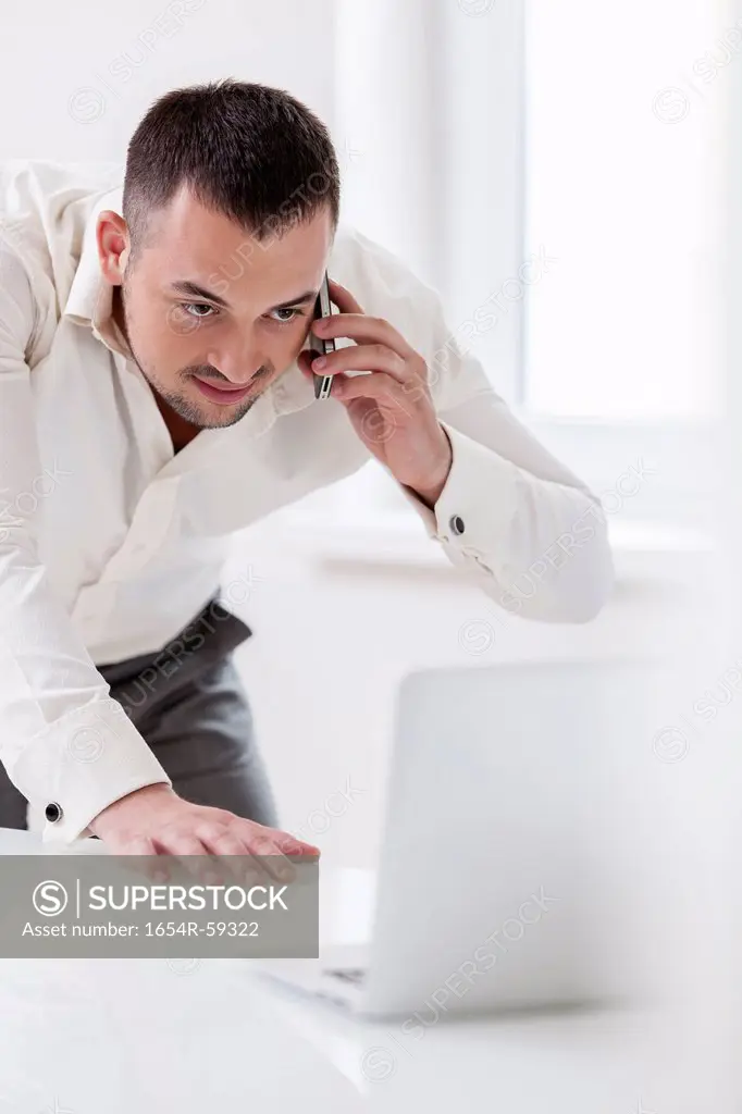 Businessman using mobile phone and looking at computer
