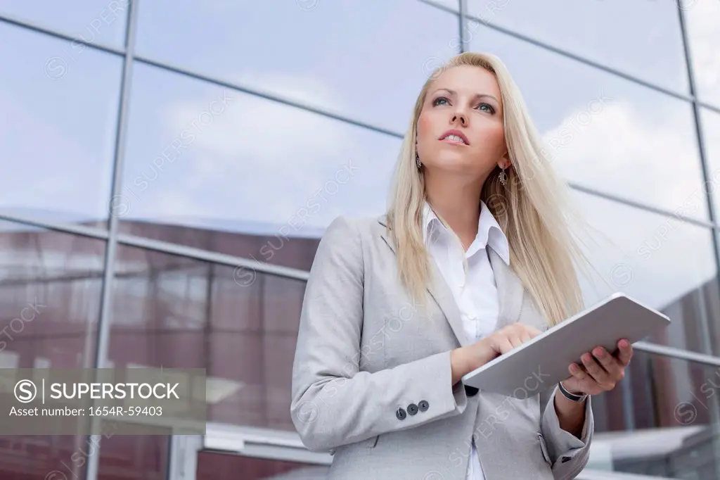 Low angle view of businesswoman holding digital tablet while looking away against office building