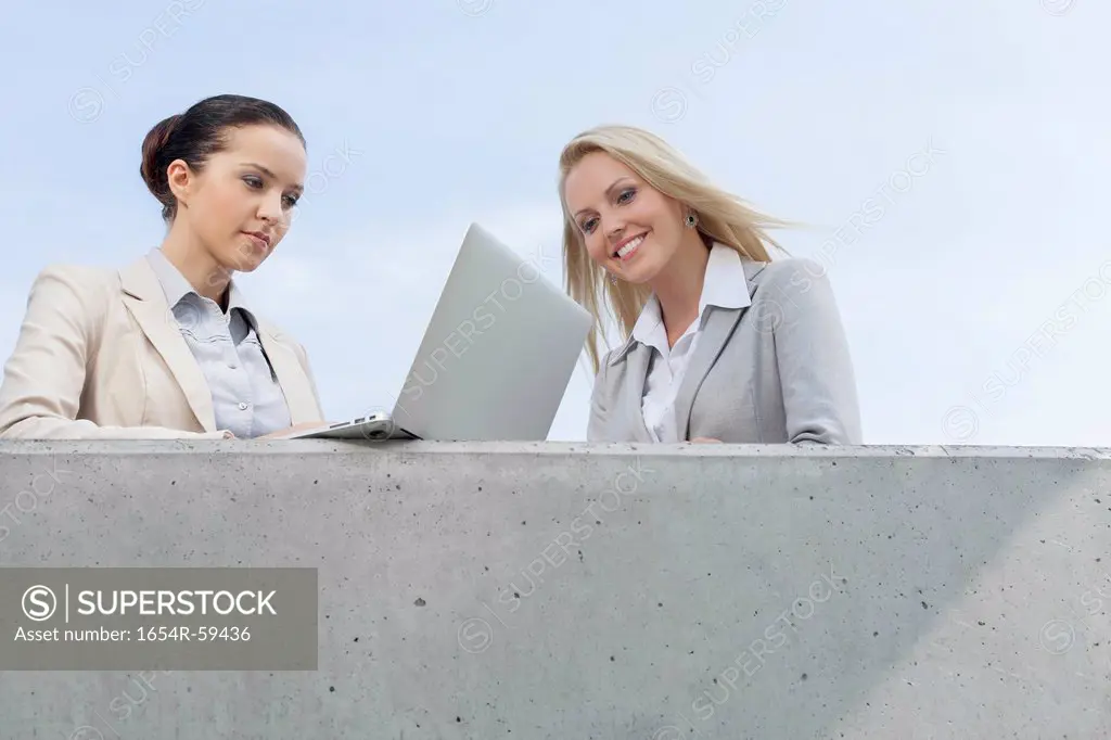 Low angle view of businesswoman using laptop while standing with colleague on terrace against sky