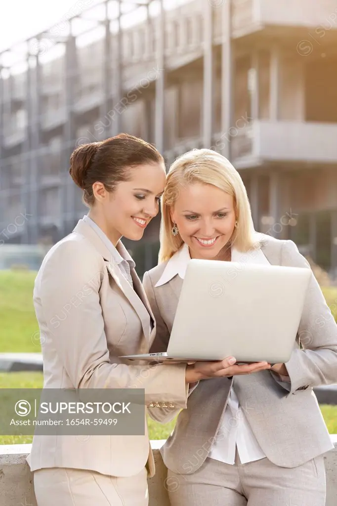Happy young businesswomen using laptop together against building