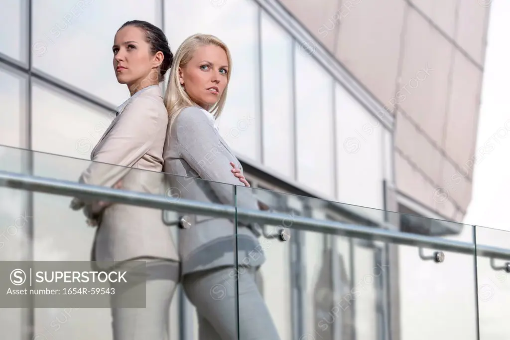 Serious young businesswomen standing back to back at office railing