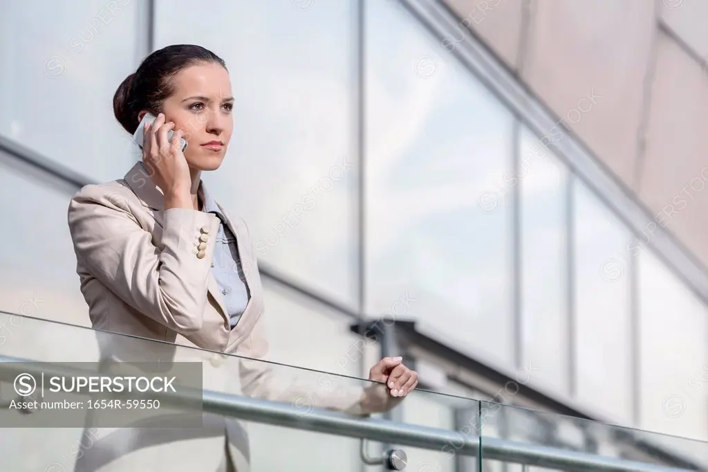 Confident young businesswoman using smart phone at office railing