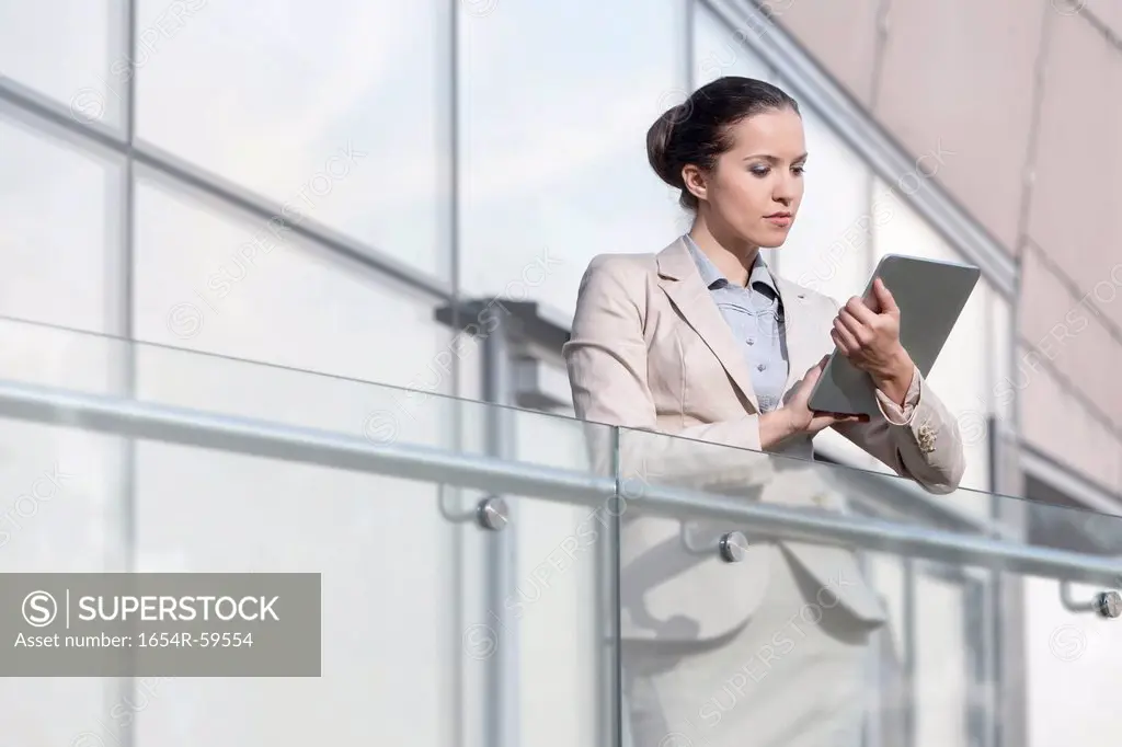 Beautiful young businesswoman using digital tablet at office railing