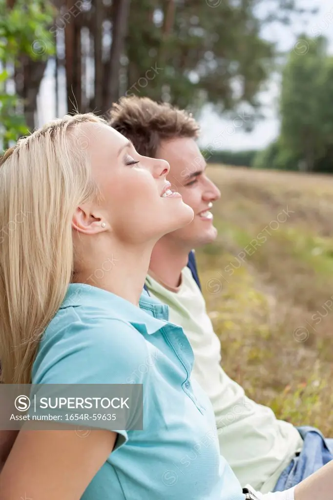 Beautiful young woman with eyes closed relaxing by man in forest