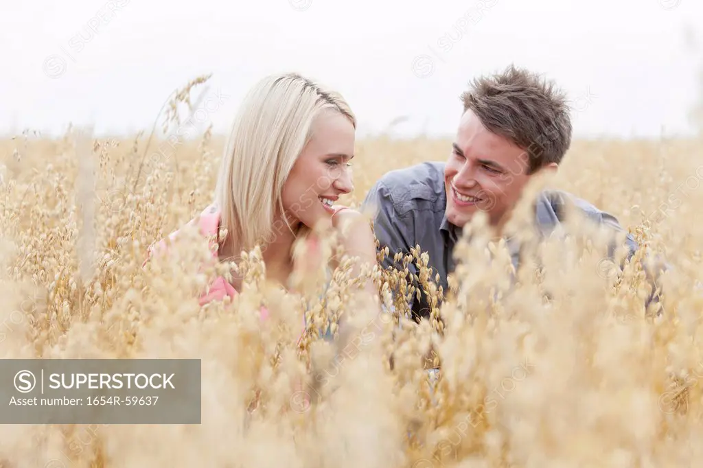 Happy man looking at woman while relaxing amidst field