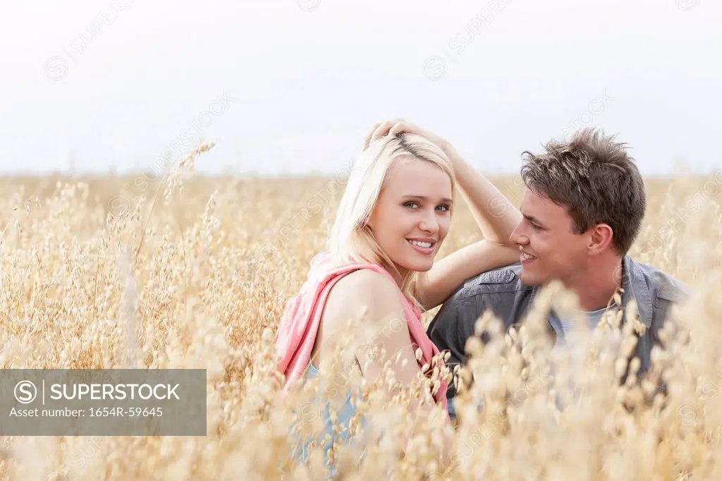 Portrait of beautiful young woman sitting with boyfriend amidst field