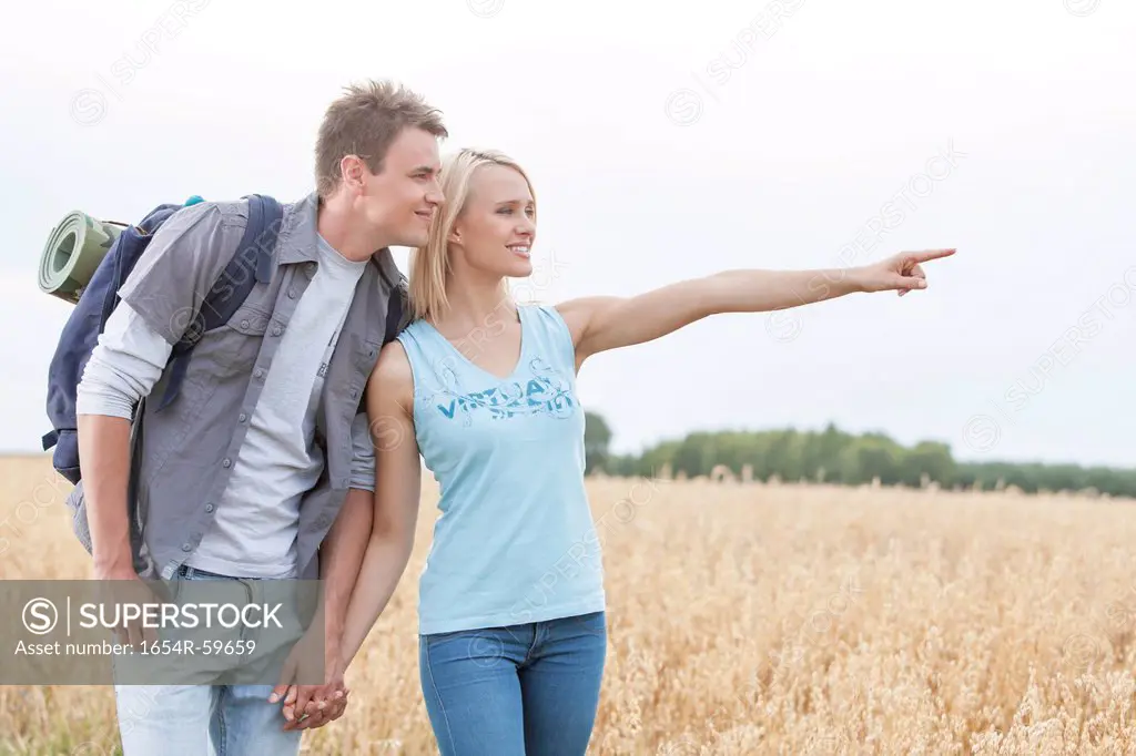 Happy female hiker showing something to man on field against clear sky