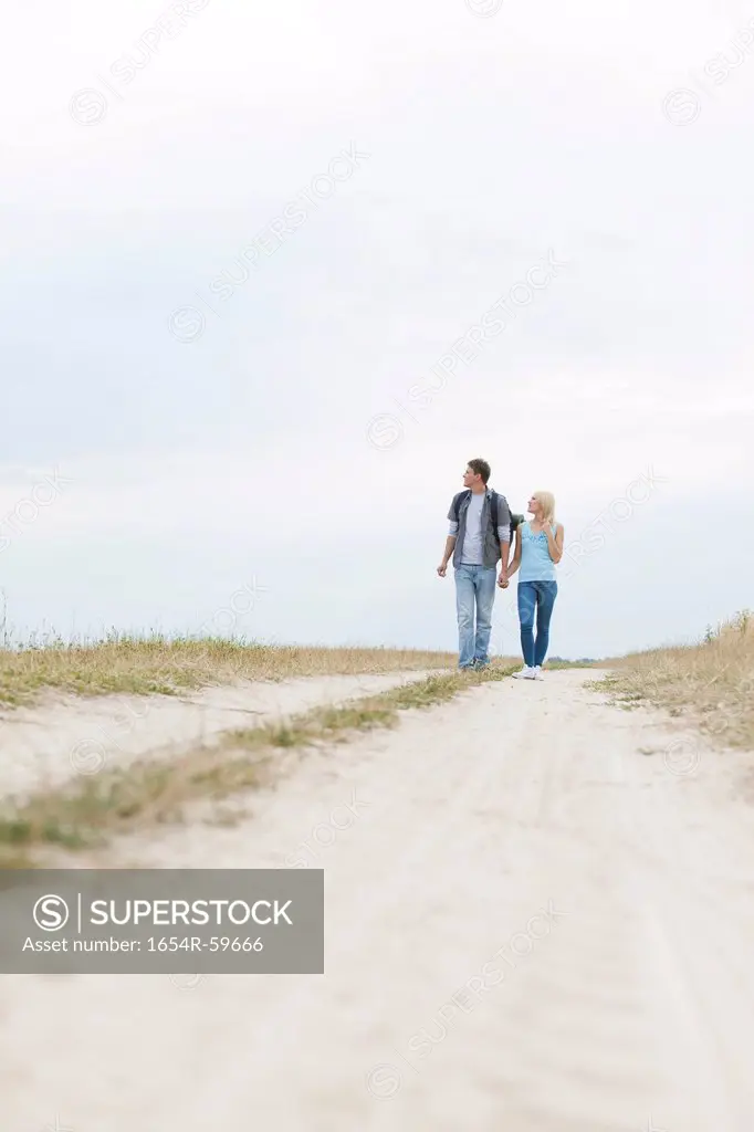 Full length of young hiking couple walking on path at field