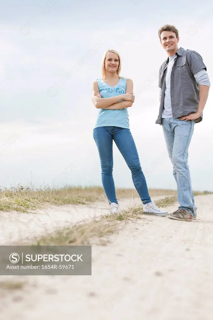 Full length portrait of young couple standing on trail at field
